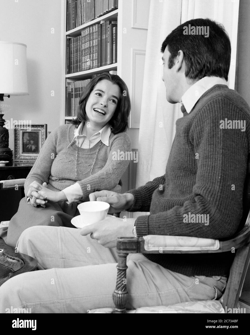 1970s COUPLE IN LIVING ROOM LAUGHING WOMAN SITTING WITH HANDS CLASPED FINGERS INTERTWINED LOOKING AT MAN HOLDING CUP AND SAUCER - s20812 HAR001 HARS PAIR ROMANCE FLIRTING OLD TIME NOSTALGIA OLD FASHION 1 COMMUNICATION LAUGH BALANCE TEAMWORK FINGERS PLEASED JOY LIFESTYLE FEMALES MARRIED SPOUSE HUSBANDS HOME LIFE COPY SPACE FRIENDSHIP HALF-LENGTH LADIES PERSONS CARING MALES NERVOUS B&W PARTNER DATING HAPPINESS CHEERFUL STRATEGY AND EXCITEMENT AT IN OPPORTUNITY SMILES CONNECTION CLASPED JOYFUL MID-ADULT MID-ADULT MAN MID-ADULT WOMAN RELAXATION TOGETHERNESS WIVES BLACK AND WHITE Stock Photo