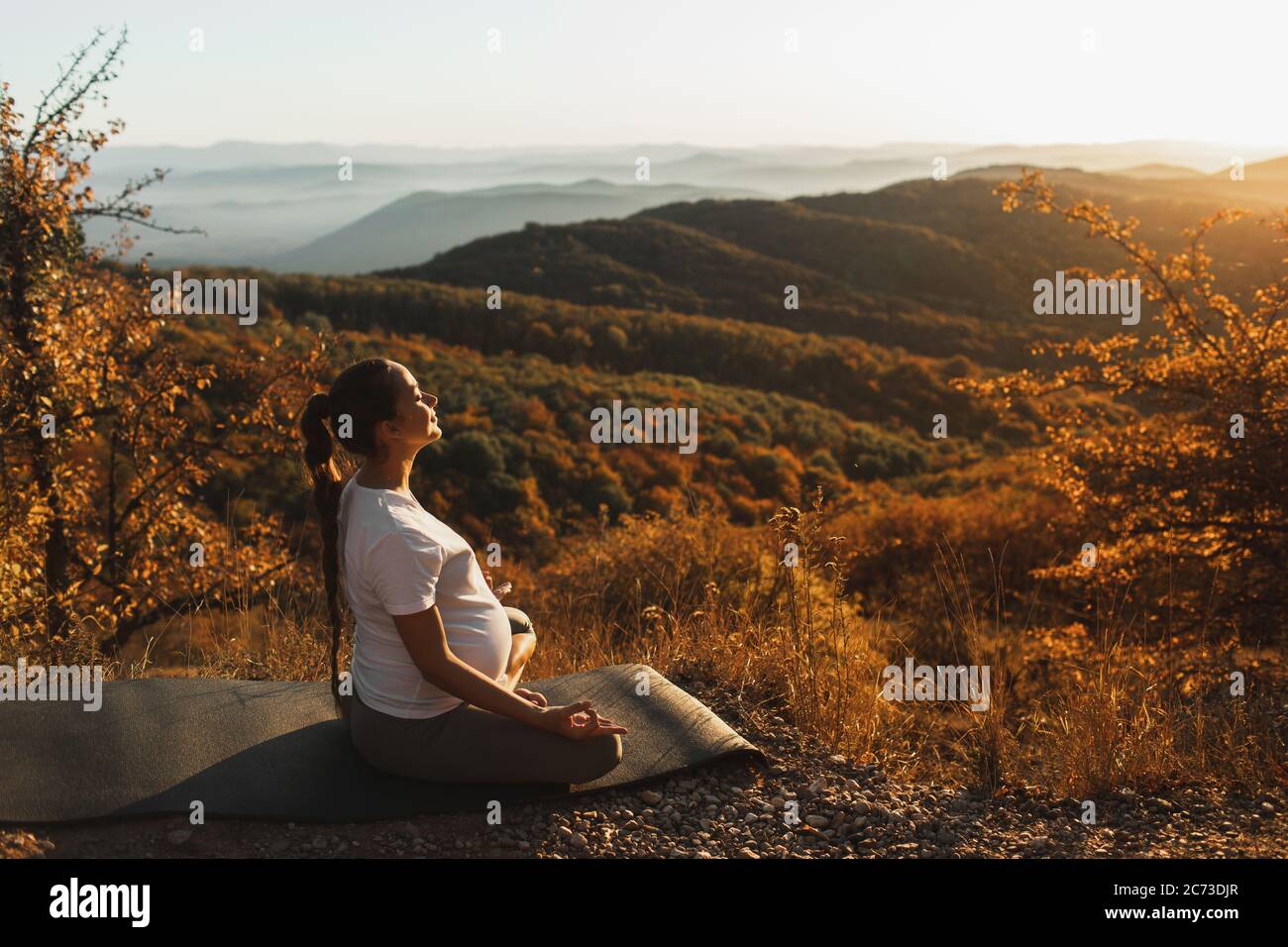 Pregnant woman in lotus position do yoga alone outdoors. Amazing autumn mountain view at sunset. Spiritual maternity concept, natural harmony. Stock Photo