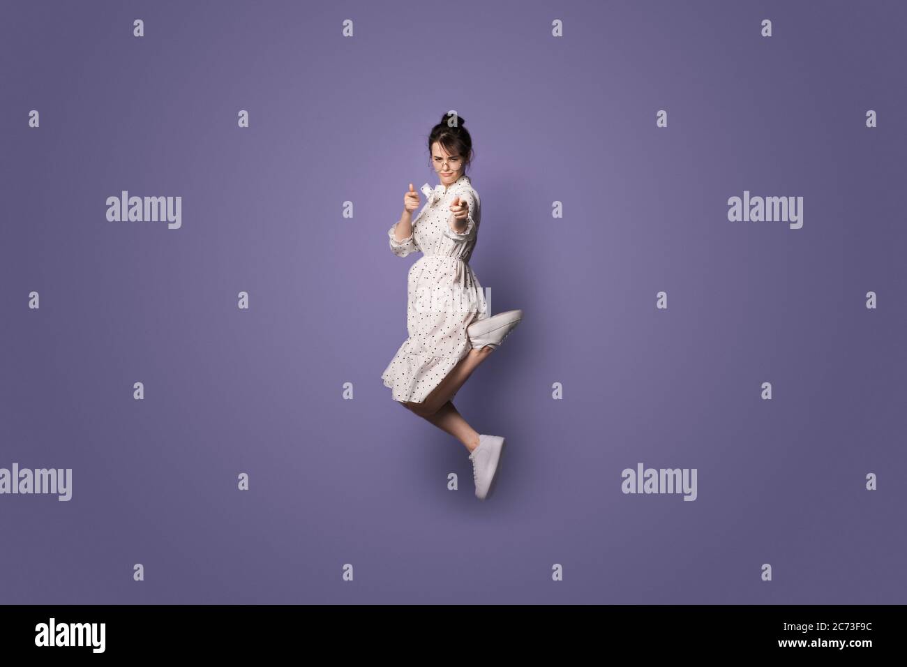 Serious caucasian woman jumping on a violet studio wall with free space and pointing at camera Stock Photo