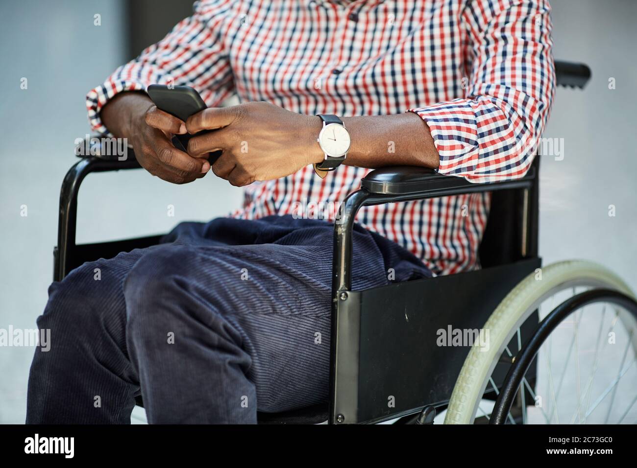 Close-up of African disabled man sitting in wheelchair and playing on his mobile phone Stock Photo