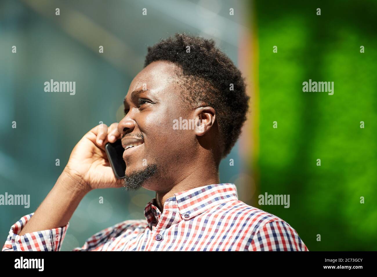African smiling man talking on mobile phone while walking outdoors Stock Photo