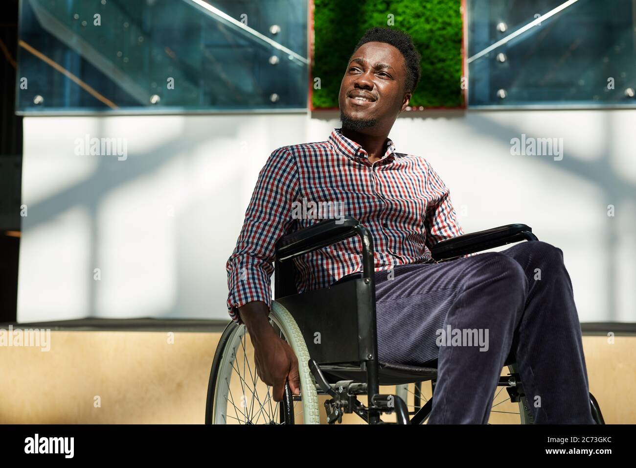 African man in wheelchair looking away and smiling at modern office Stock Photo