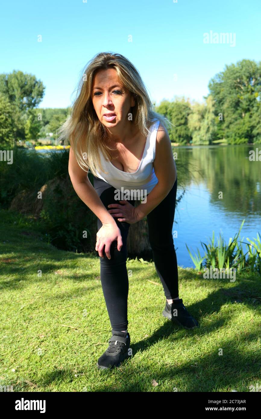 Blonde woman does fitness exercises during a workout in nature. Well-being and healthy lifestyle. Background deliberately blurred. Stock Photo