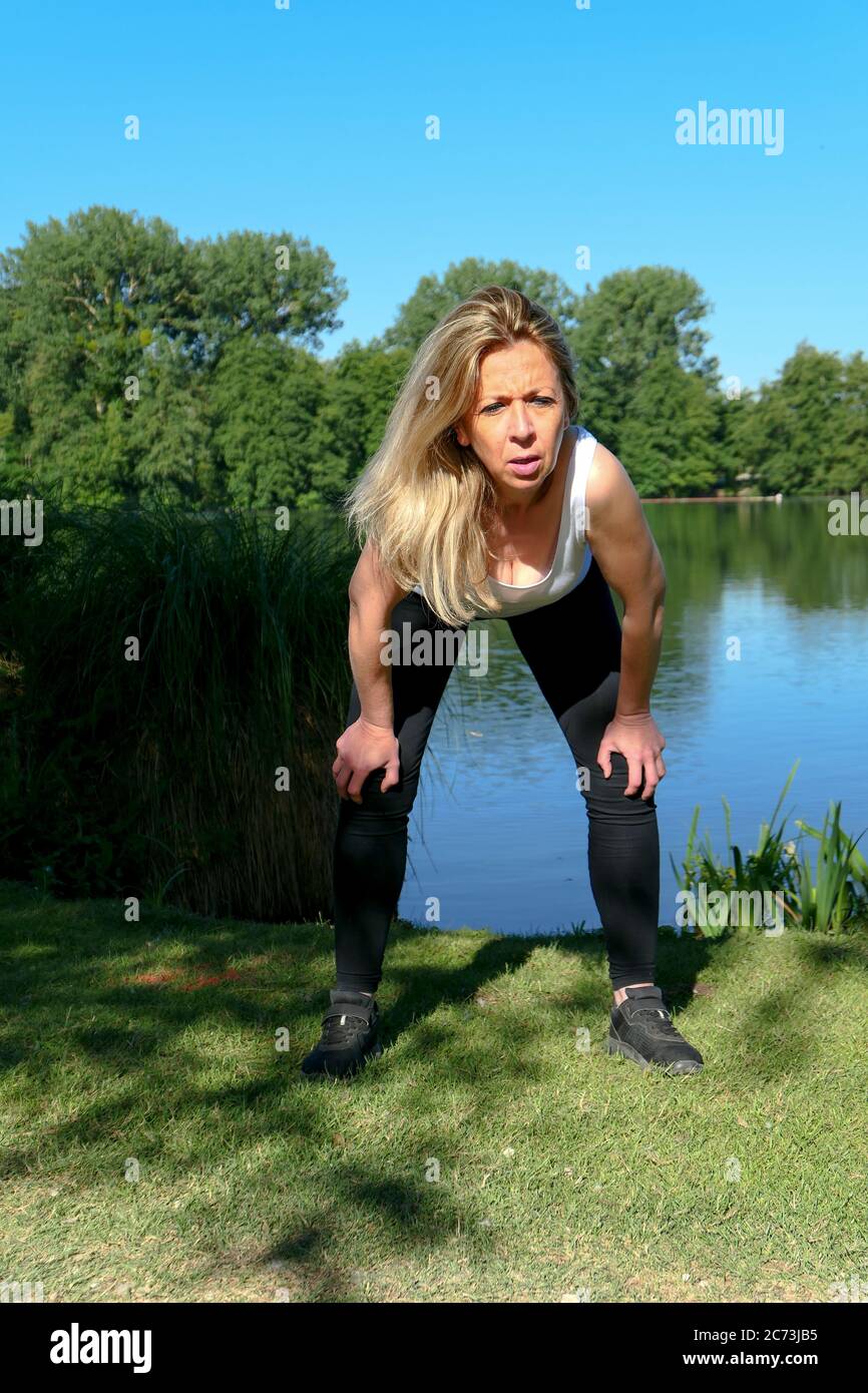 Blonde woman does fitness exercises during a workout in nature. Well-being and healthy lifestyle. Background deliberately blurred. Stock Photo
