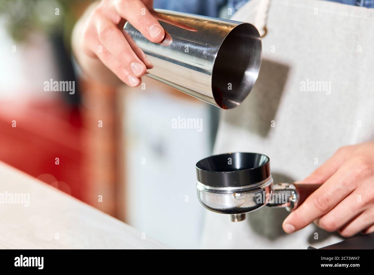 close up of delicate hands of male barman keeping metal coffee pot, pouring ground coffee into tamper, blurred background Stock Photo