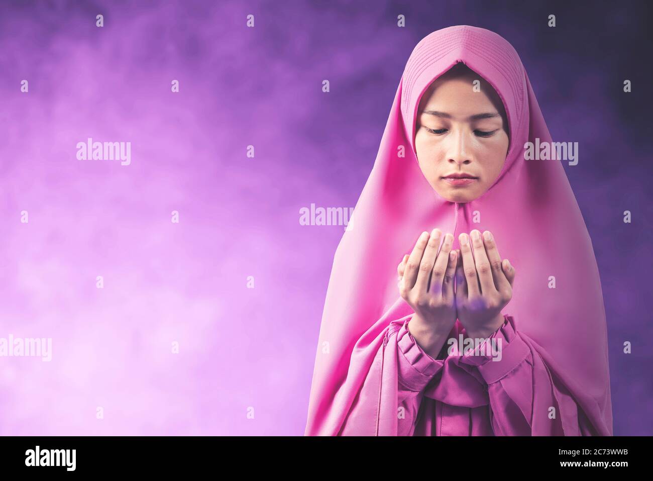 Asian Muslim woman in a veil standing while raised hands and praying ...