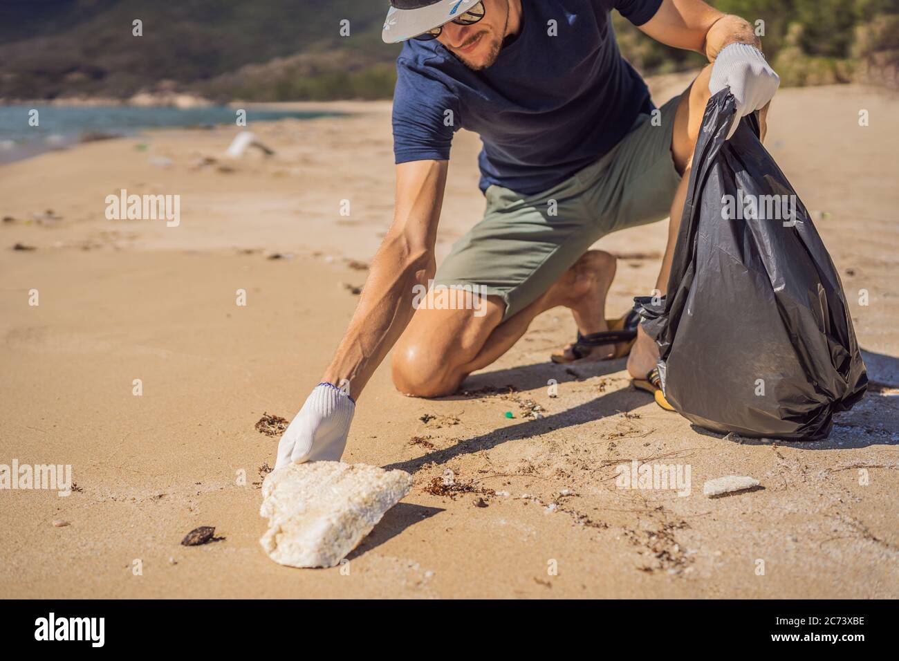 Man in gloves pick up plastic bags that pollute sea. Problem of spilled