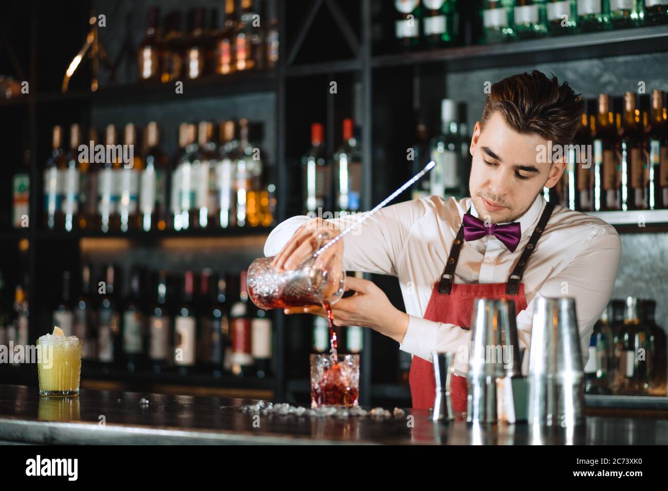 https://c8.alamy.com/comp/2C73XK0/professional-bartender-in-uniform-doing-show-of-his-work-holding-two-parts-of-metal-shaker-in-his-hands-and-pouring-a-cocktail-shelves-full-of-bottl-2C73XK0.jpg