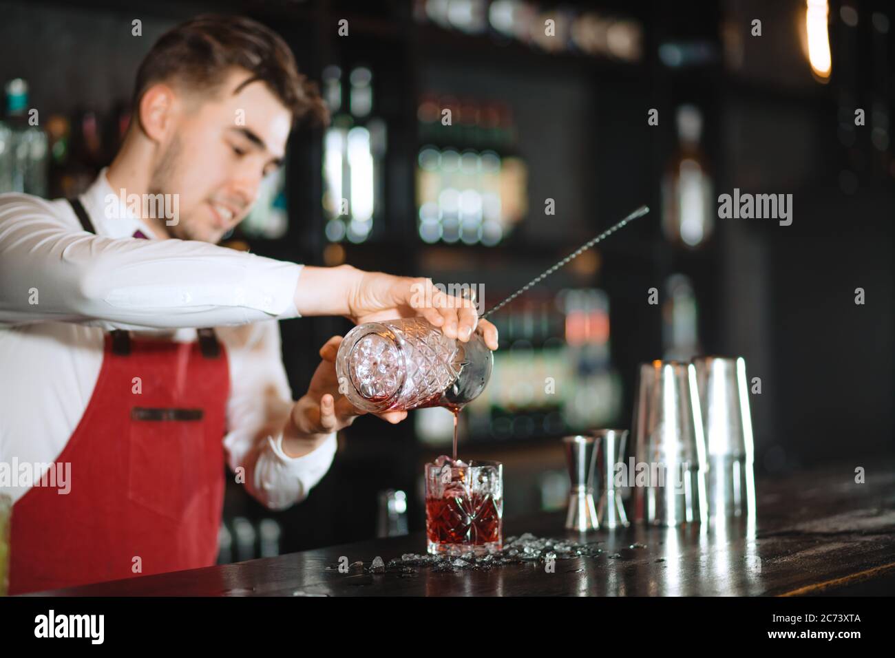 The bartender man pours ruby cocktail into crystal glass. Bar, Restaurant Beverage and Service concept. Stock Photo