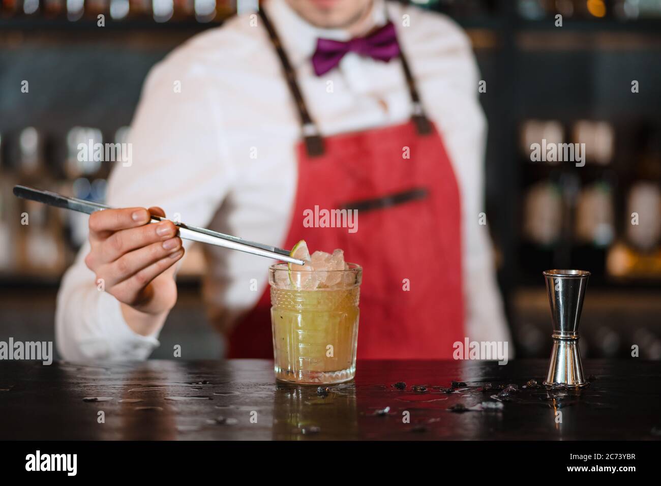 Bartender finishes decoration of his cocktail with ice cubes and lime slice using tweezers Stock