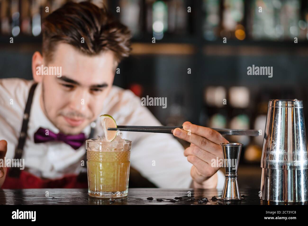 Bartender finishes decoration of his cocktail with ice cubes and lime slice using tweezers Stock