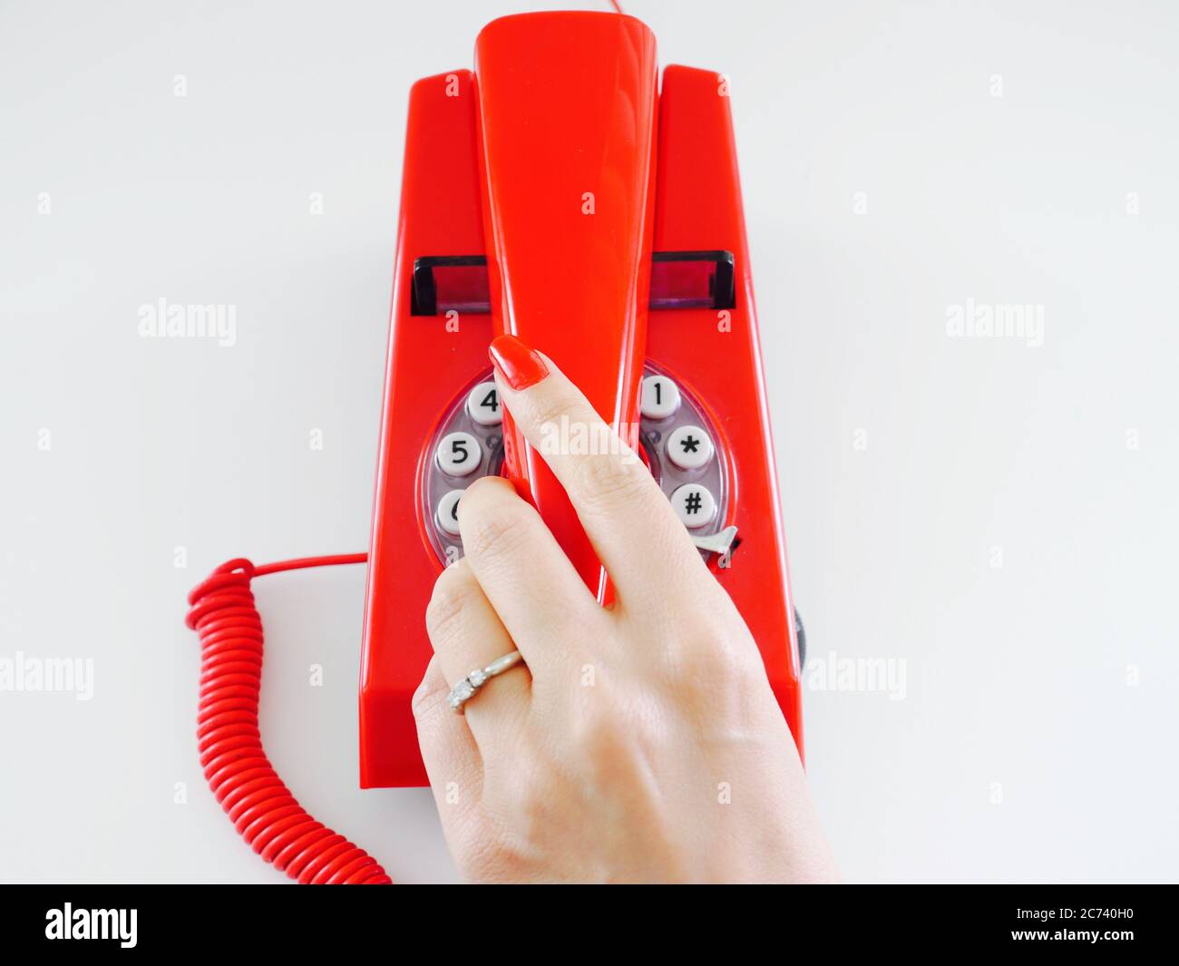 Female hand with red manicured nails and engagement ring holds the receiver on a red retro telephone Stock Photo