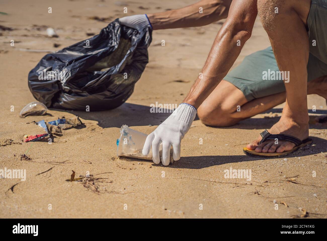 Man in gloves pick up plastic bags that pollute sea. Problem of spilled