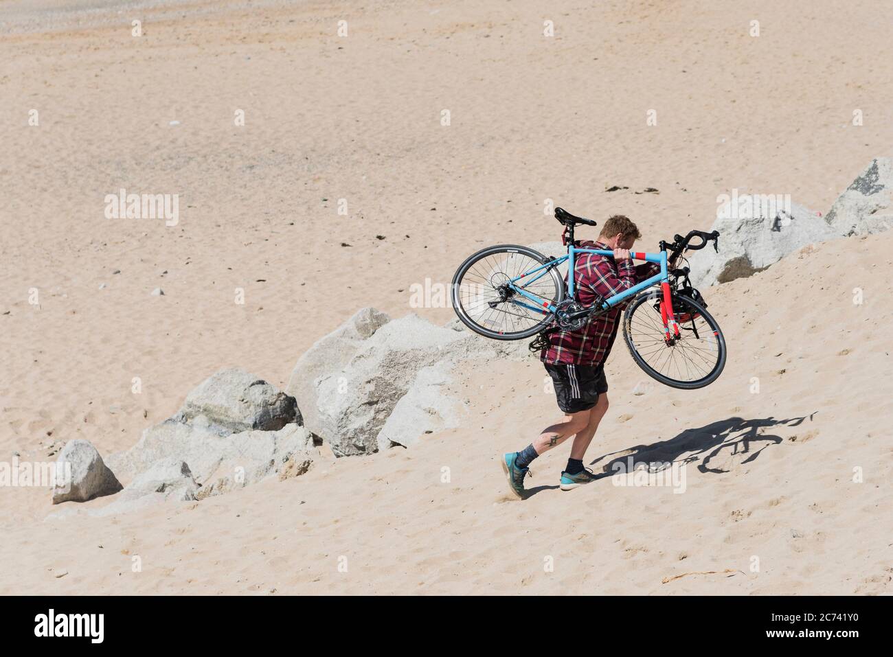 A cyclist carrying his bicycle across soft sand on Fistral Beach in Newquay in Cornwall. Stock Photo