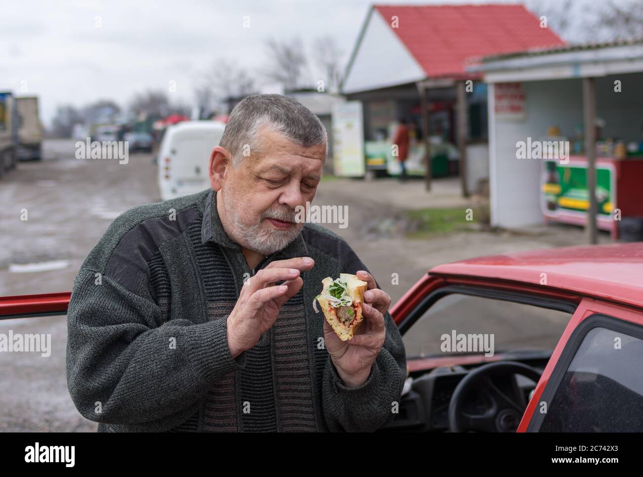 Senior driver holding street food (lyulya kebab in lavash) near his car while standing on a back road in Ukraine Stock Photo