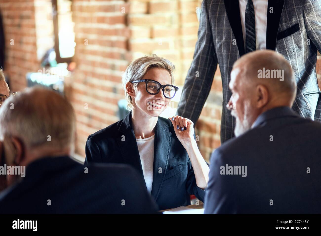 Focused on blonde caucasian woman in glasses smile, talk between backs of two men Stock Photo