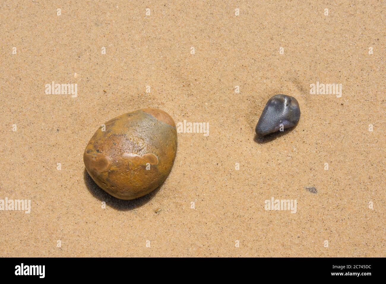 A group of pebbles pebbles resting on a background of flat water washed sand Stock Photo