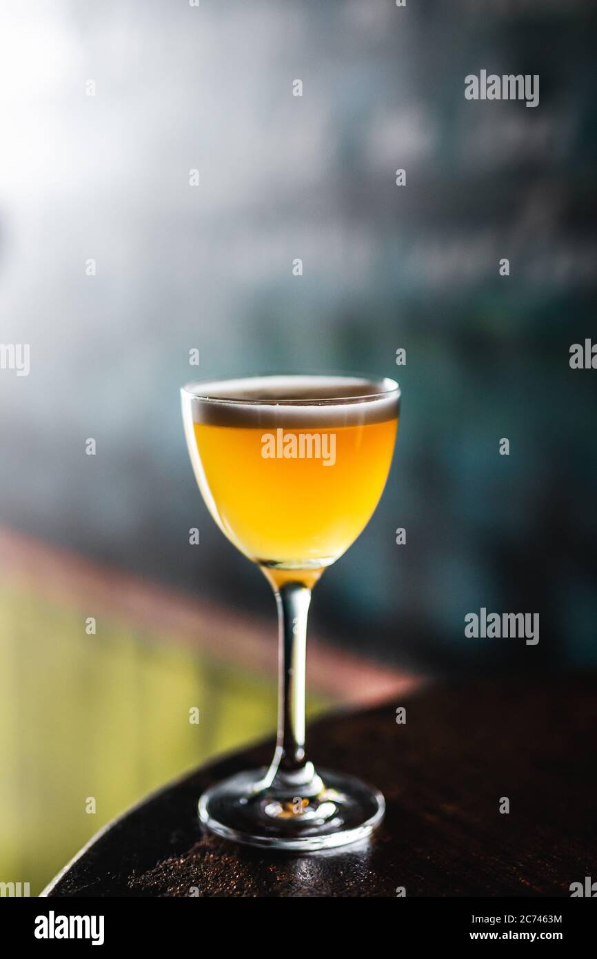 A sour cocktail in a nick and nora glass with orange peel garnish on