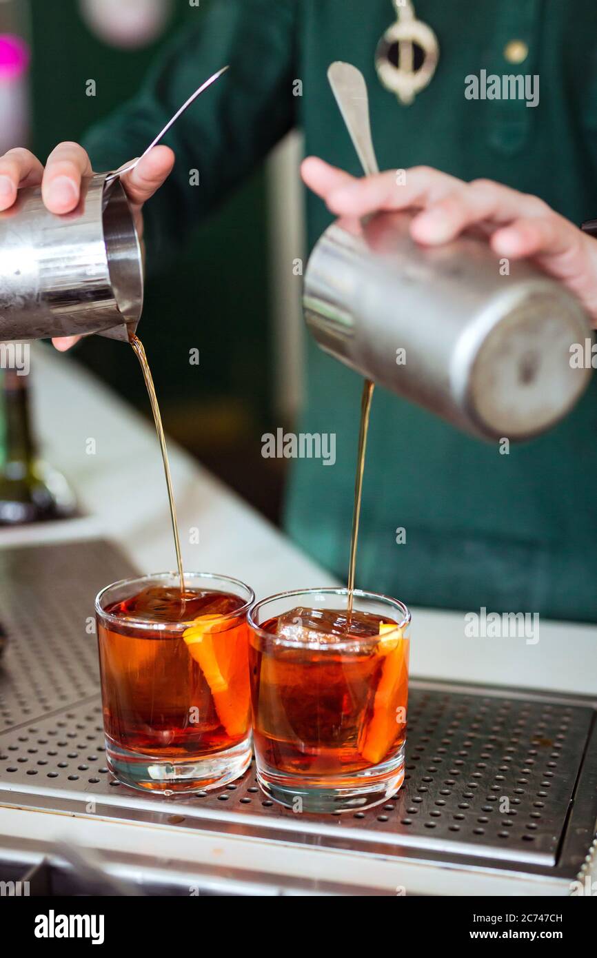 Bartender making a negroni cocktail at the bar pouring a drink from a