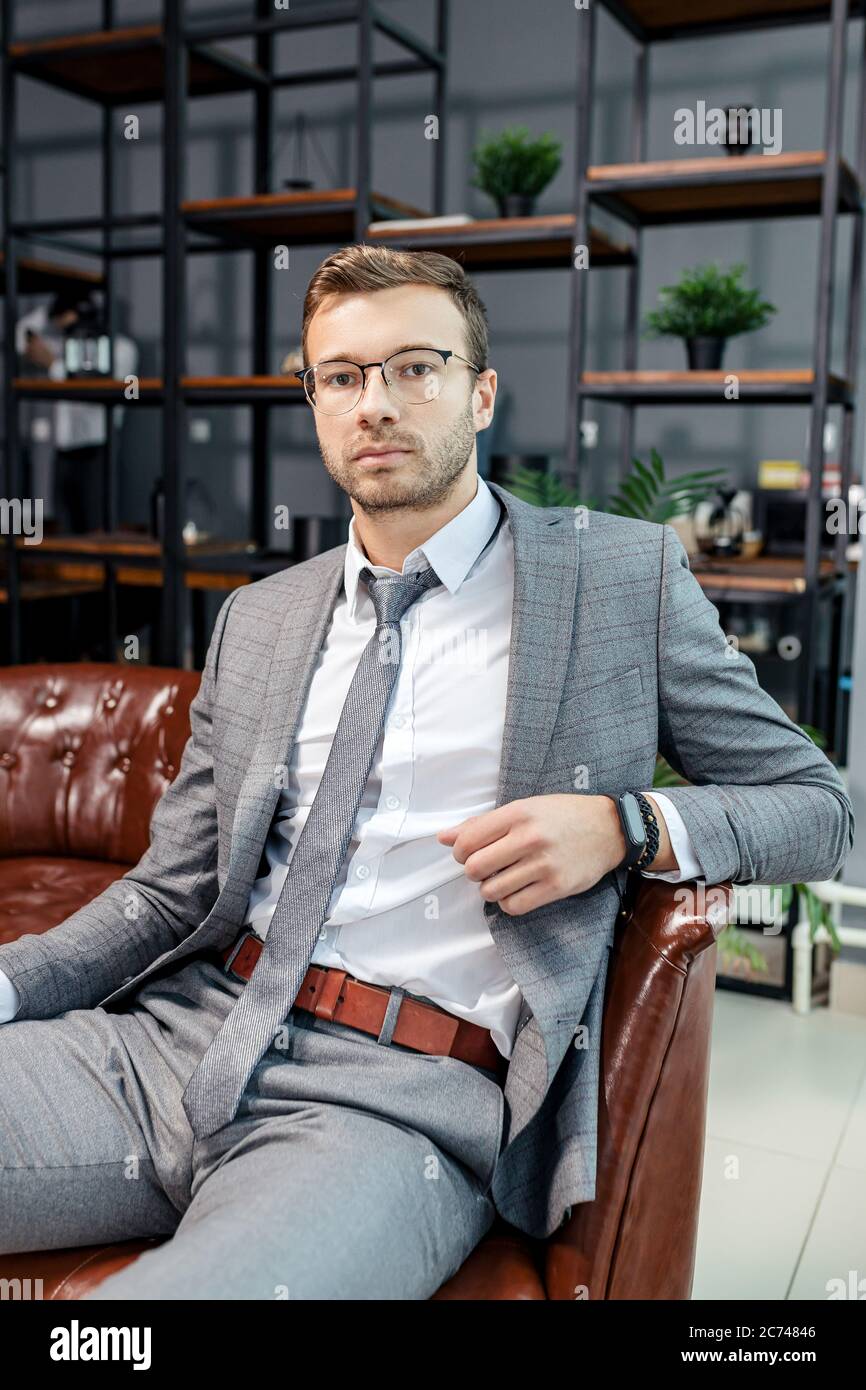 confident young handsome business man in stylish grey tuxedo sitting in leather chair and look at camera Stock Photo Alamy