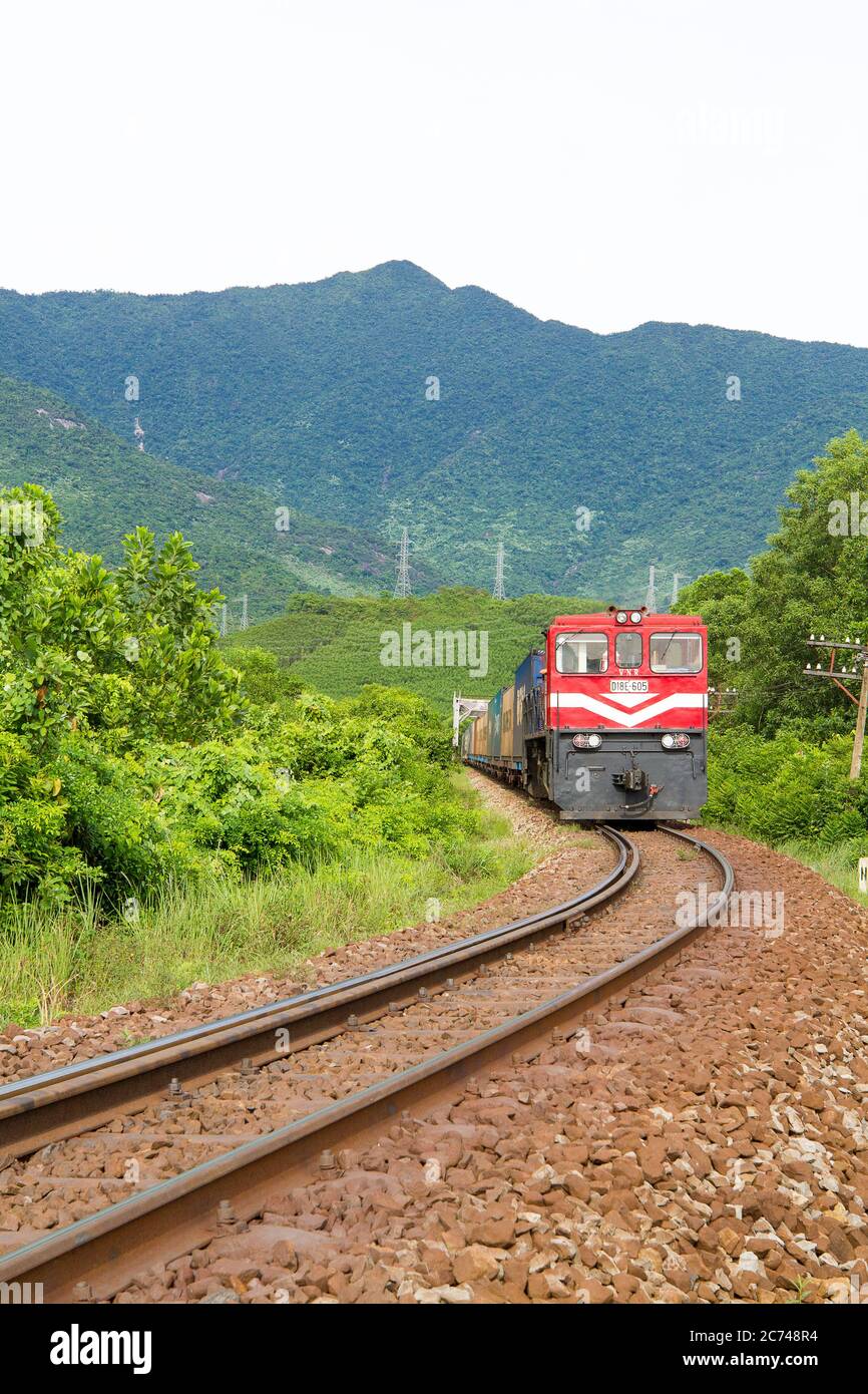 Train is running on railway with mountain view, trees and yellow gravel in Hue - Vietnam Stock Photo