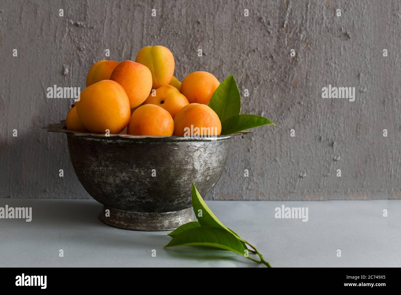 Apricots in a Vintage Bowl with Cinnamon Sticks and Leaves on a Grey Concrete Background Stock Photo