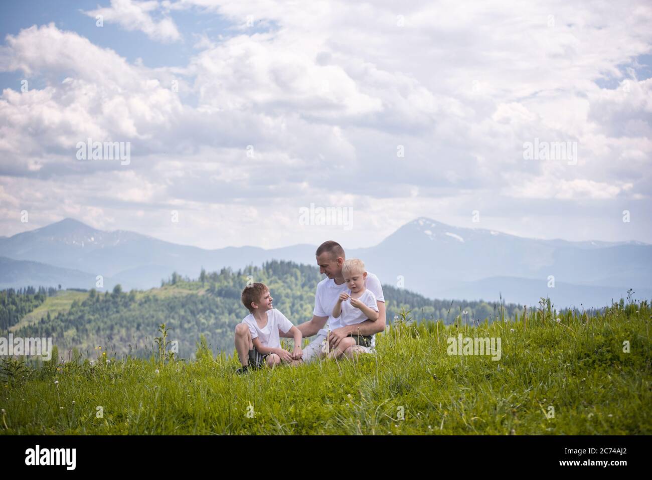 Happy father with his two young sons sitting on the grass on a ...