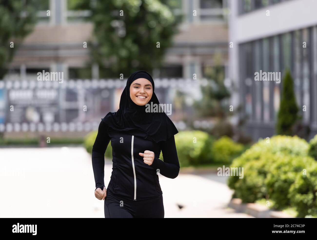 smiling arabian girl in hijab and sportswear jogging outside Stock Photo