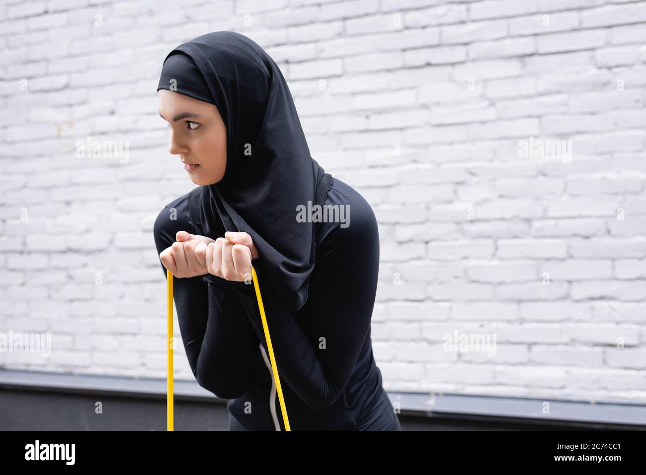 arabian girl in hijab exercising with resistance band near brick wall Stock Photo
