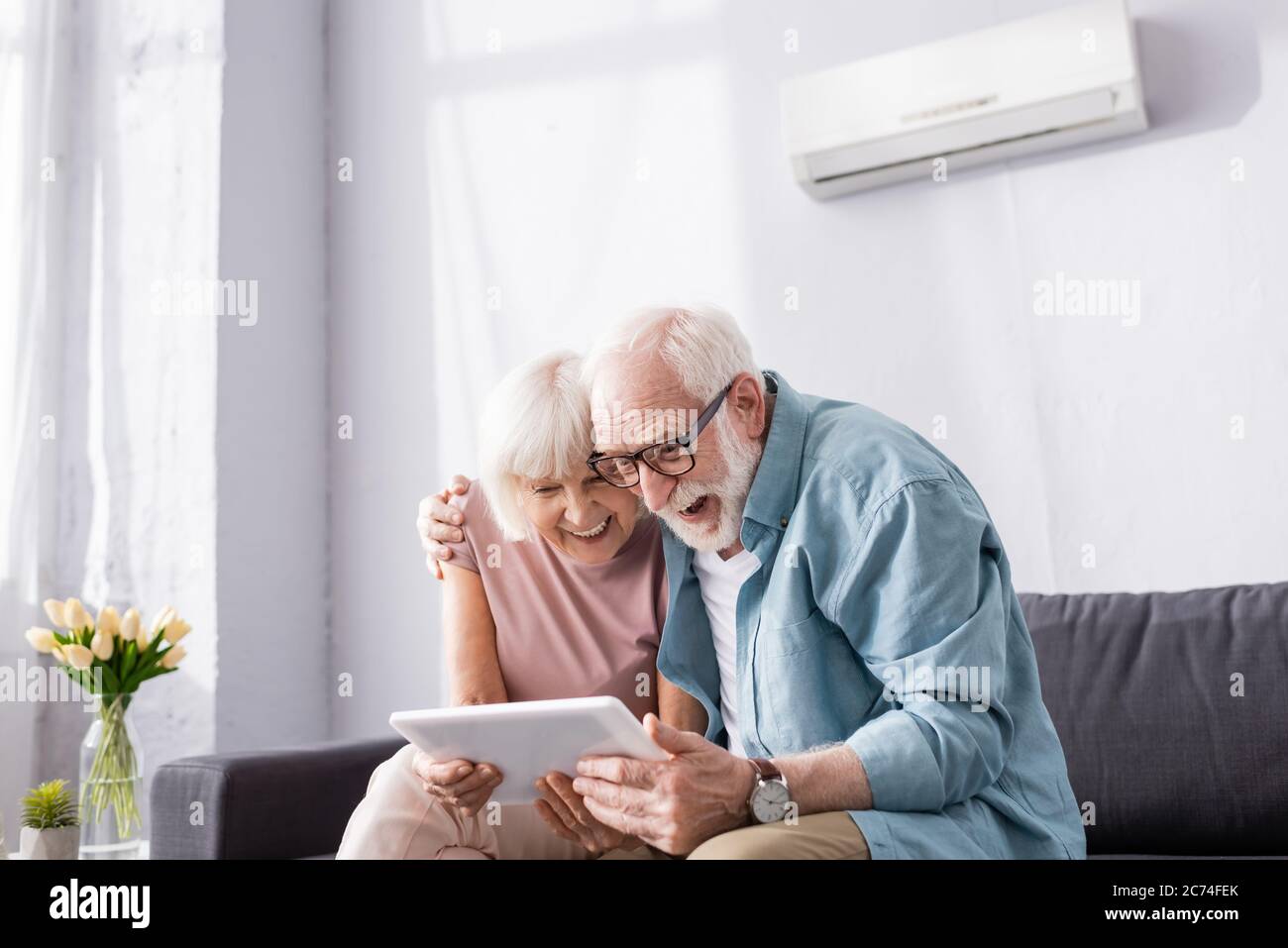 Positive senior coupe using digital tablet on couch at home Stock Photo