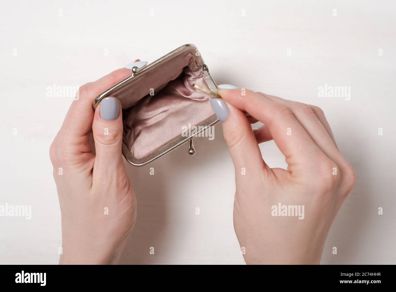 Hand puts a coin in an empty open metal purse on a light background ...