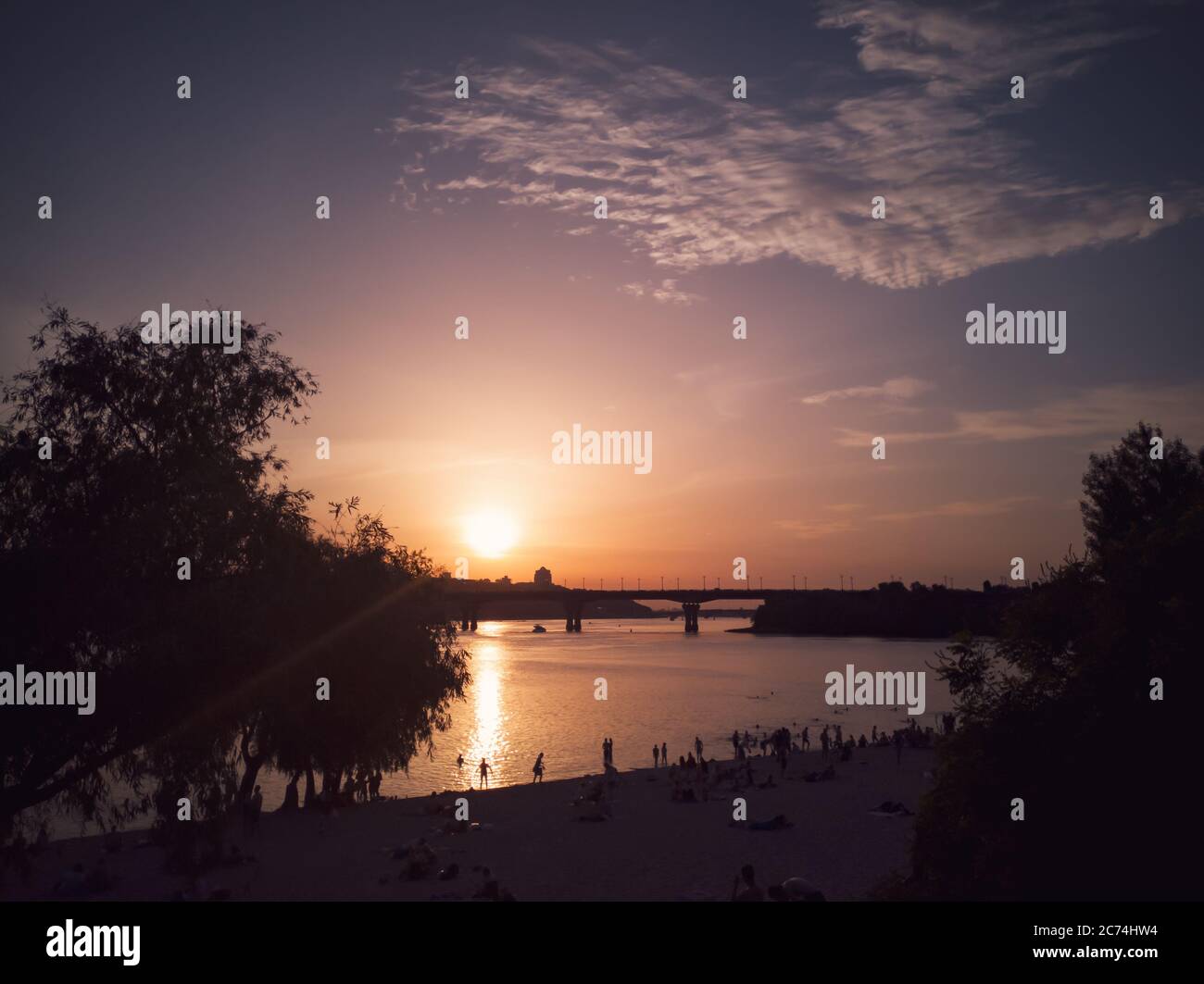 People swimming and having rest on the beach on the left bank of the Dnipro river in Kyiv on summer evening. Urban cityscape with motherland monument. Stock Photo