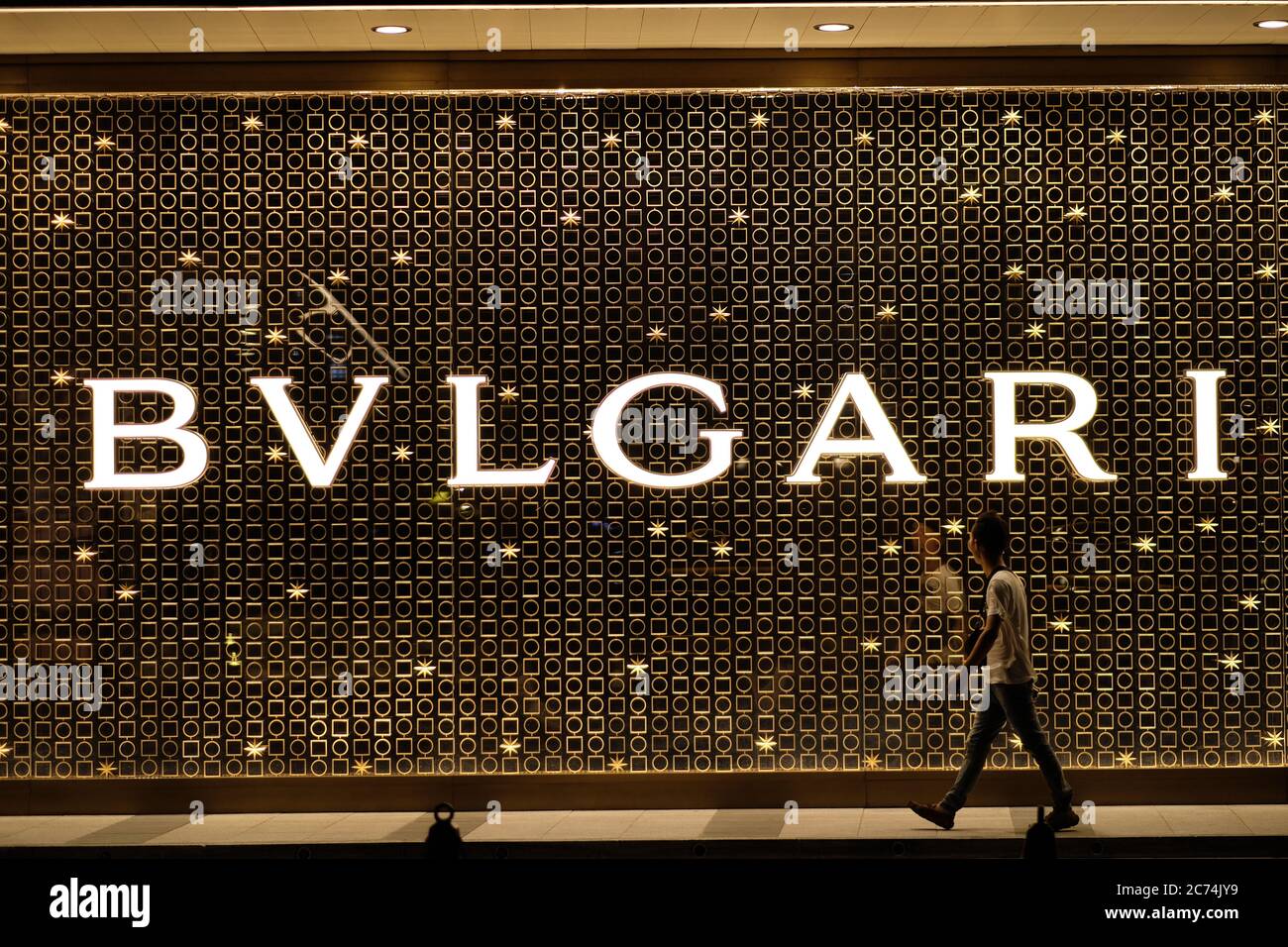 one young man walking past and looking at Bvlgari's big golden shining logo on the wall outside store.  An Italian luxury brand. Stock Photo