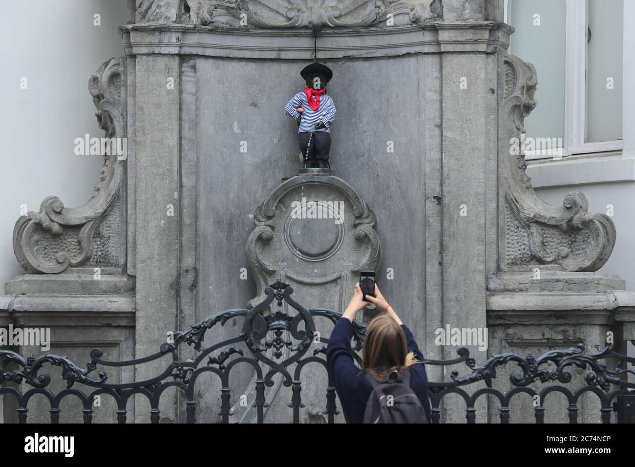 Brussels, Belgium. 14th July, 2020. A visitor takes photos of the Manneken-Pis which wears a suit with beret and baguette in Brussels, Belgium, July 14, 2020. Manneken-Pis, the symbol of Brussels folklore, gets costumes at major events. He wore a suit with beret and baguette on Tuesday to commemorate the French national day which falls on July 14 every year. Credit: Zheng Huansong/Xinhua/Alamy Live News Stock Photo
