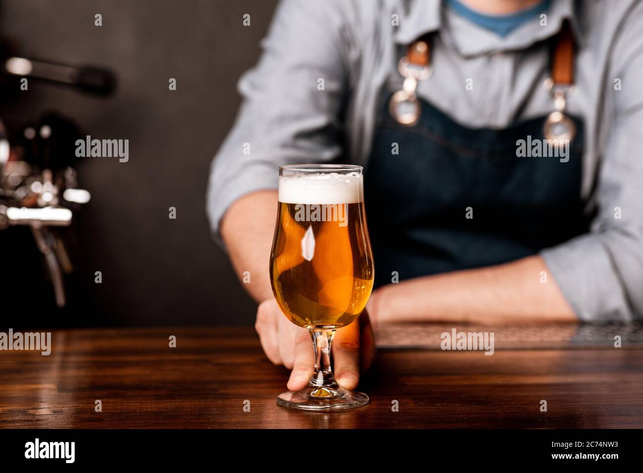 Pint of beer on bar in traditional style of pub. Guy in apron gives glass of light ale Stock Photo