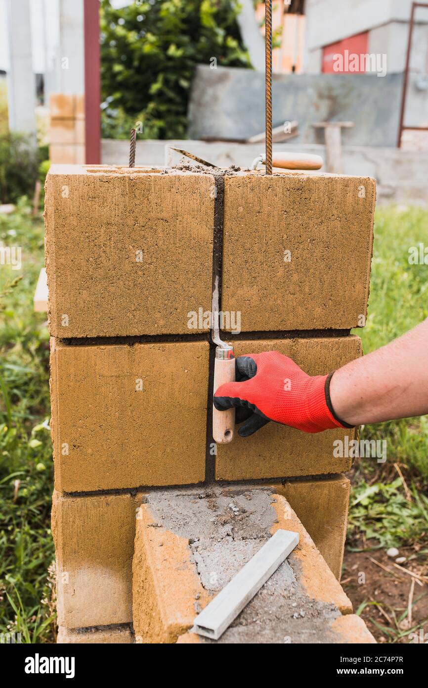 A professional bricklayer builds pillars for a stone fence from cement