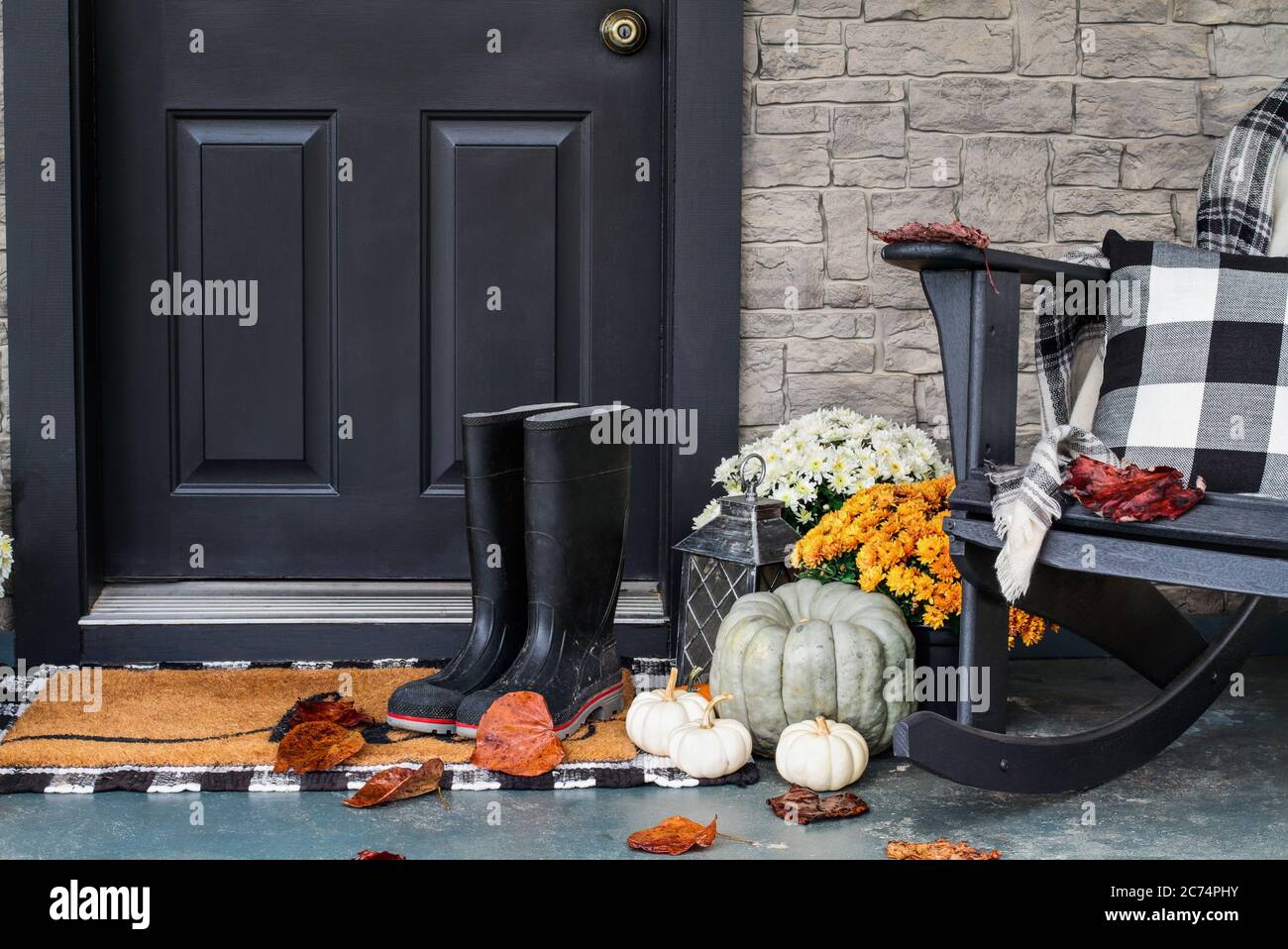 Traditional style front porch decorated for autumn with rain boots, heirloom gourds,  white pumpkins, mums and rocking chair with buffalo plaid pillow Stock Photo