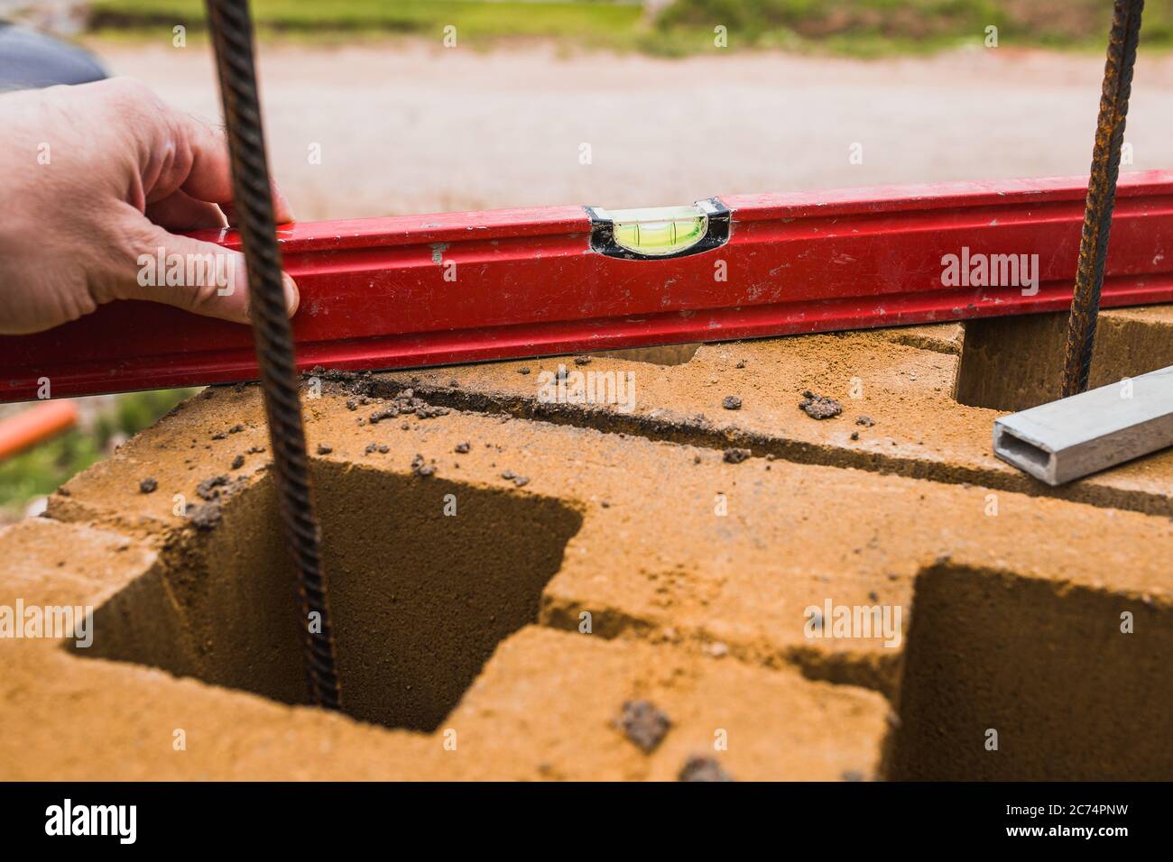 A professional bricklayer builds pillars for a stone fence from cement