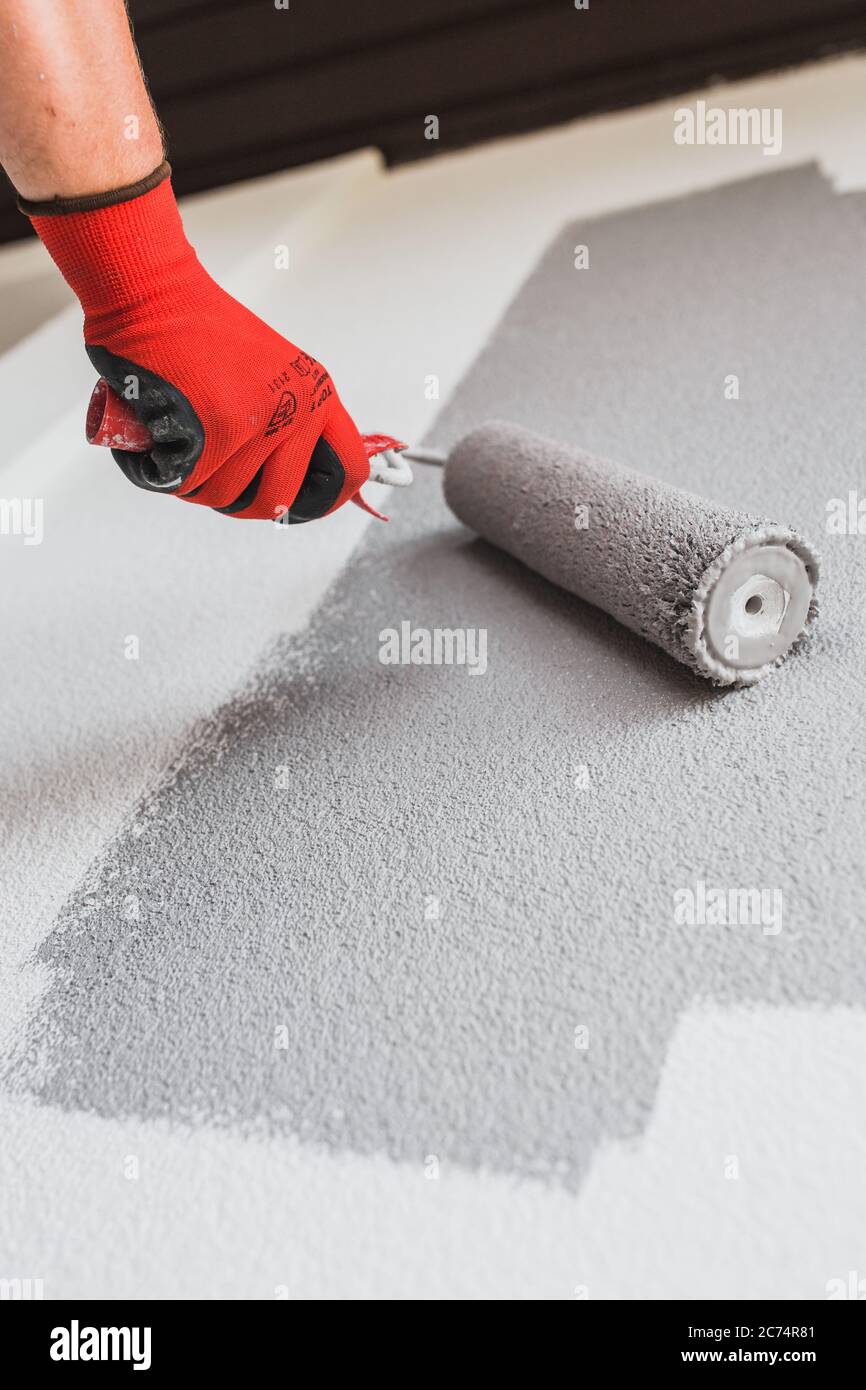 Paint roller paints the white wall in gray painting works outside the