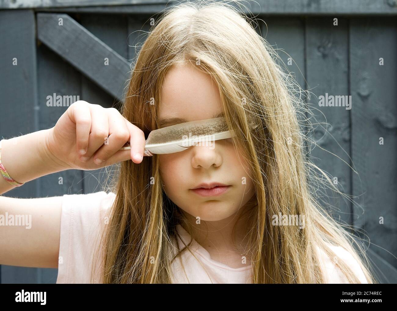 A blonde girl holding a feather over her eyes Stock Photo