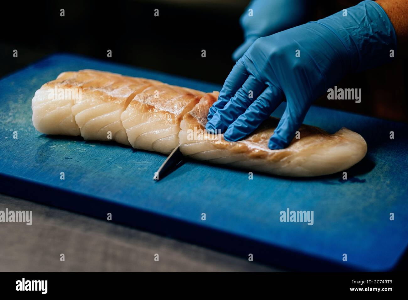 close-up on hands in blue latex gloves cutting raw fish on chopping board Stock Photo