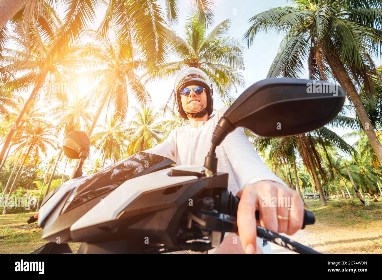 Happy smiling and screaming male tourist in helmet and sunglasses riding motorbike  scooter during his tropical vacation under palm trees Stock Photo - Alamy