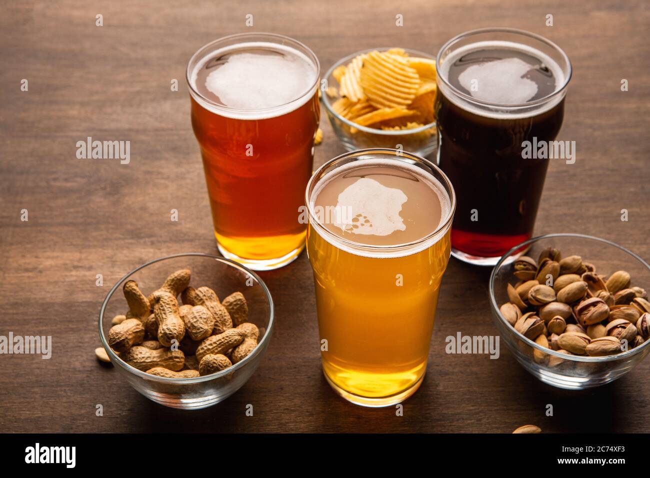 Dark amber and unfiltered beer in glasses. Pistachios, nuts and chips in plates on table Stock Photo