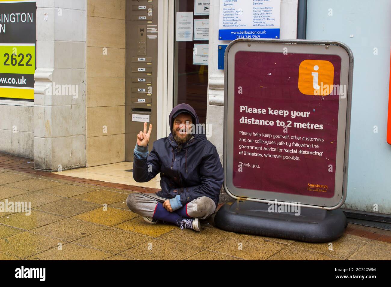 8 July 2020. A young homeless man sits begging outside a Sainsbury's supermarket in downtown Sheffield England on a wet day during the Covid 19 health Stock Photo