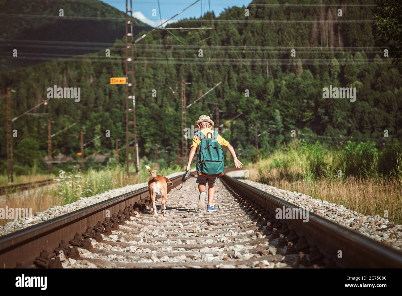 Little boy walking with big backpack and his beagle dog run on railway Stock Photo