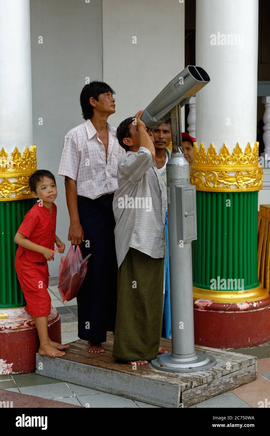 Young boy and a man viewing the top of the Shwedagon Pagoda in Myanmar via large fixed binoculars telescope Stock Photo