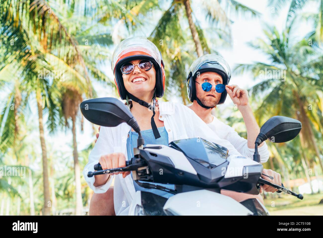 Happy smiling and screaming male tourist in helmet and sunglasses riding motorbike  scooter during his tropical vacation under palm trees Stock Photo - Alamy