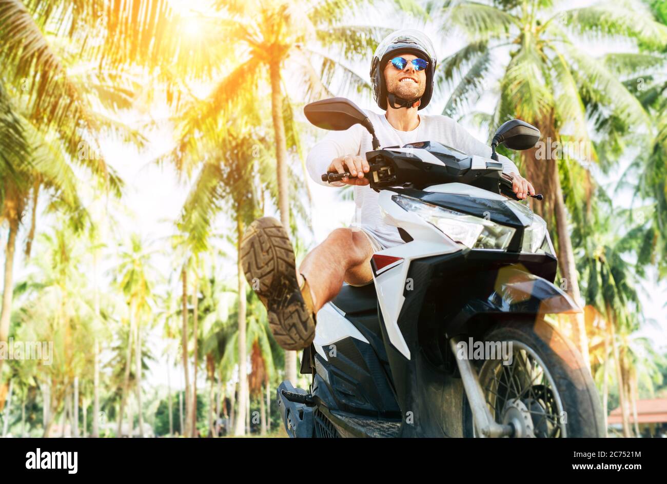 Happy smiling and screaming male tourist in helmet and sunglasses riding motorbike  scooter during his tropical vacation under palm trees Stock Photo - Alamy