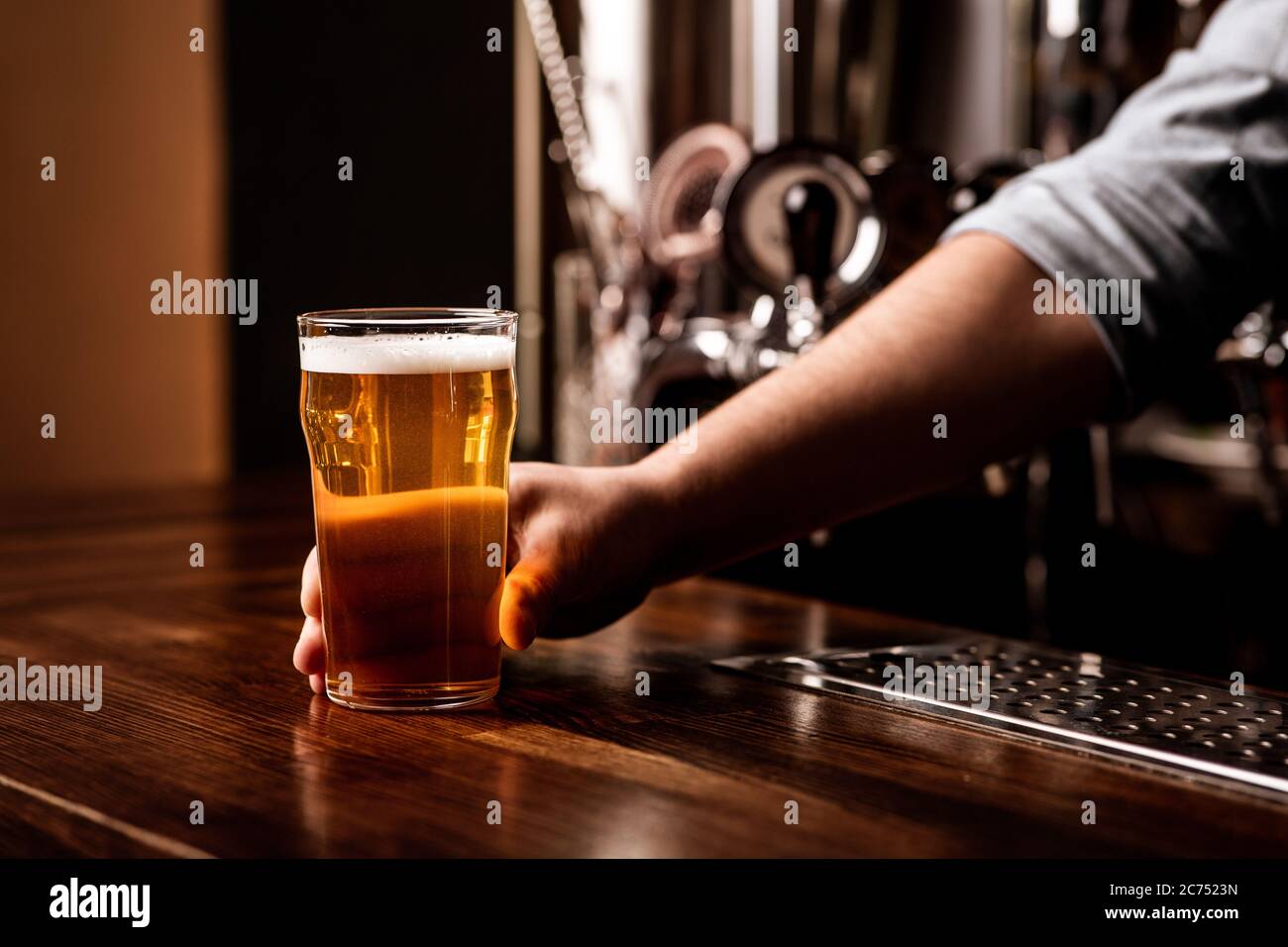 Craft beer for regular client. Bartender gives glass of light lager in interior of pub Stock Photo