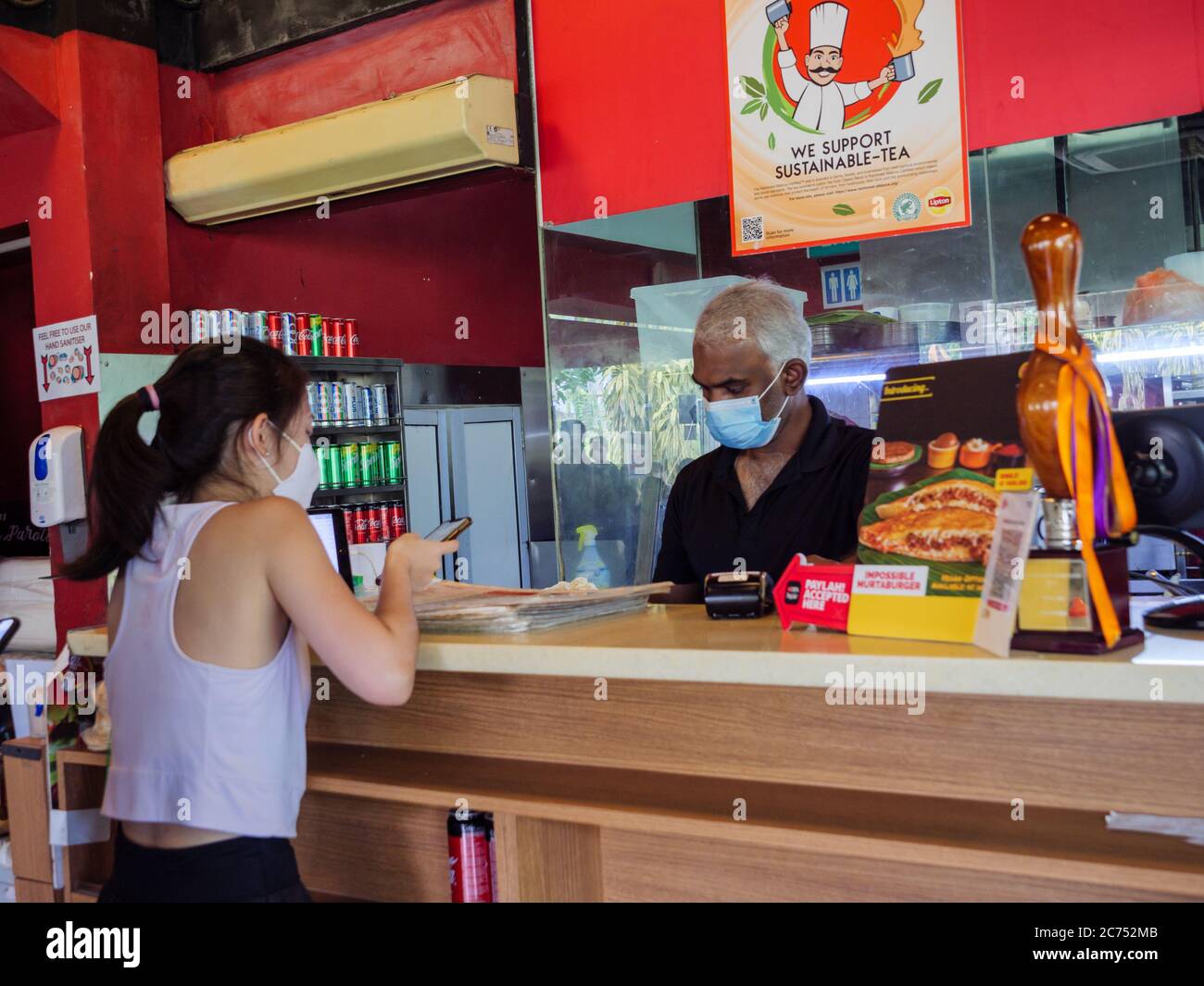 SINGAPORE – JULY 10 2020 – A customer at the Springleaf Prata Place Indian restaurant in Singapore wears a protective mask and pays via mobile phone c Stock Photo